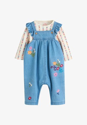 Denim overalls med flæsebesatte stropper, knapper og farverig blomsterbroderi. Bærer en langærmet skjorte med striber.