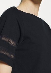 Černý top s kulatým výstřihem a krátkými rukávy, s krajkovými zdobeními na rukávech. Hladký materiál, pohodlný střih a jednoduchý design.