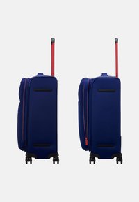 Valigia rigida blu con zip e maniglia rossi, dotata di quattro ruote e un design snello. Presenta dettagli neri sui lati.