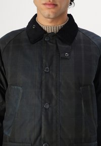 Black plaid jacket made of a smooth texture with a corduroy collar, featuring snap buttons and two front pockets.