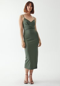 Olivengrünes, eng anliegendes Midikleid mit Spaghettiträgern, herzförmigem Ausschnitt und gedrehtem Vorderteil. Verfügt über eine glatte, matte Textur.