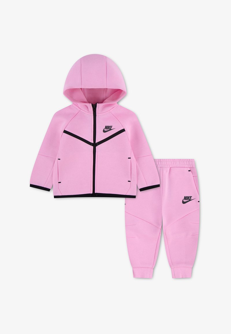 Ροζ παιδική φόρμα Nike με ζακέτα με κουκούλα και φερμουάρ και ταιριαστό παντελόνι με ελαστική μέση, με μαύρο λογότυπο και λεπτομέρειες περιγράμματος.