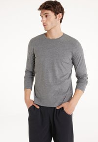 Šedá dlouhá rukávová košile z měkké texturované látky s kulatým výstřihem a manžetami. V kombinaci s tmavými kalhotami, čímž vytváří ležérní vzhled.