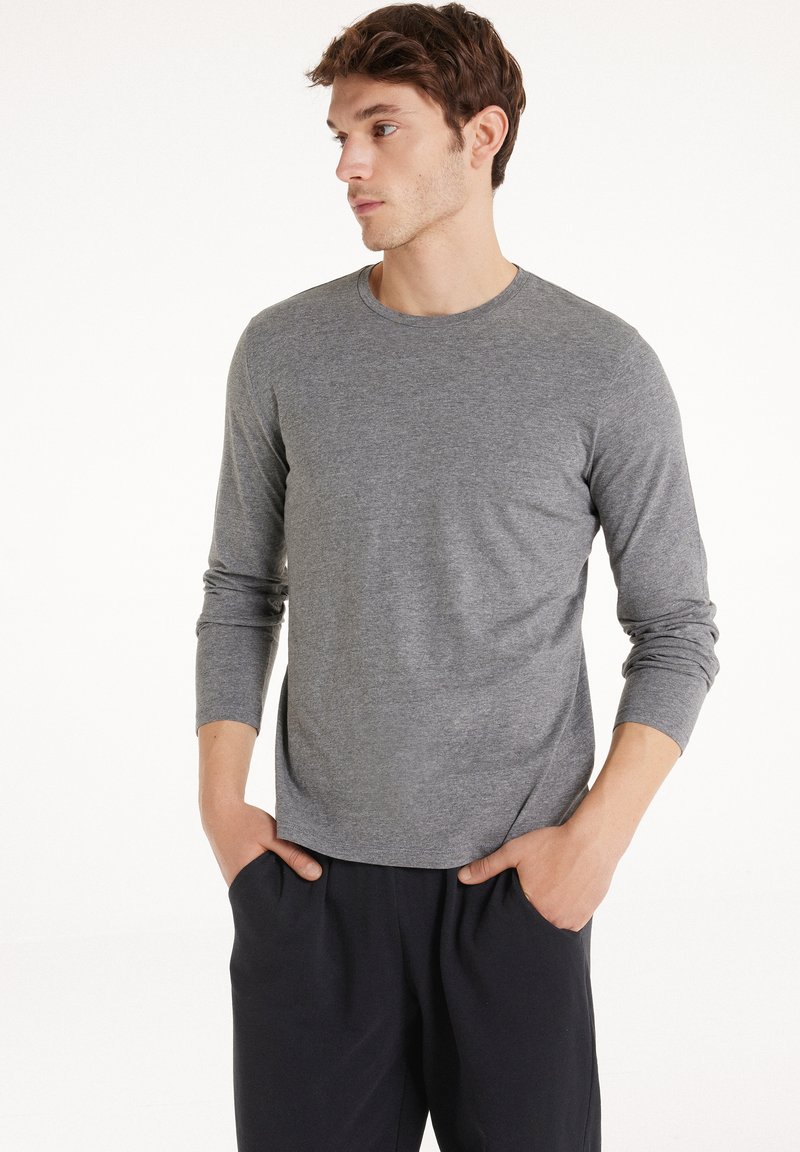 Šedá dlouhá rukávová košile z měkké texturované látky s kulatým výstřihem a manžetami. V kombinaci s tmavými kalhotami, čímž vytváří ležérní vzhled.