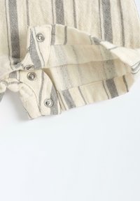 Tissu rayé aux couleurs gris et crème, avec des boutons-pression sur l'ourlet. La texture semble douce et tissée, avec des motifs de fils visibles.