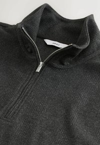 Hallhalli hallitusest zip-up fleece pullover halliküpsega, tekstuurse kangaga, kõrge kaelusega ja hõbedasest metallist tõmblukuga. Silt on nähtav kaela sees.