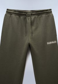Olivgrüne Sweatpants aus weichem Material, mit einem elastischen Bund und Kordelzug, sowie einem Logodruck auf dem linken Oberschenkel.
