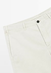 Beige Baumwollhose mit Knopfverschluss, Gürtelschlaufen und Seitentaschen. Der Stoff hat eine glatte Textur und ein lässiges Design.