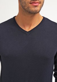 Pull à col en V bleu marine en tissu tricoté, doté d'une coupe ajustée et d'un col côtelé, idéal pour un style décontracté.