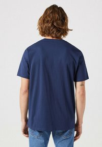 Marineblauw T-shirt met korte mouwen, eenvoudig ontwerp, van katoen, met een relaxte pasvorm, een ronde hals en een gladde textuur. Achteraanzicht, gedragen met blauwe jeans.