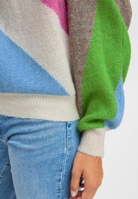 Pull en laine coloré avec des motifs géométriques roses, verts, bruns et bleus. Texture douce avec un ourlet côtelé et des manches surdimensionnées.