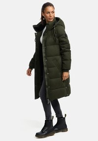 Oliven grøn quiltet lang parka med hætte, sidelommer, lynlåslukning og mærkeakkenter. Sammen med sorte snørebåndsstøvler.