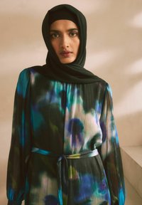 Robe en chiffon fluide et multicolore avec des motifs bleus, verts et violets ; les manches longues et une ceinture assortie mettent en valeur la silhouette.
