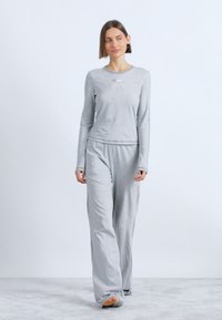 Svijetlosiva loungewear set koji se sastoji od majice s dugim rukavima i labavih hlača, izrađen od mekog, teksturiranog pamučnog materijala, s diskretnim brendiranjem.