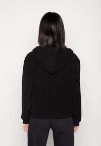 Czarna bluza z polaru o teksturowanej powierzchni, z dużym kapturem i długimi rękawami. Mankiety i dół wykończone są kontrastowym, gładkim materiałem.