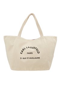 Bolso de lona beige con correas de tela dobles. La parte frontal presenta un texto negro en negrita: "Karl Lagerfeld Paris 21 Rue St-Guillaume." Diseño simple.