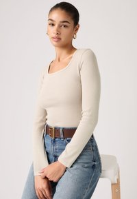 Μπεζ μακρυμάνικη ριμπ μπλούζα με τετράγωνο ντεκολτέ, συνδυασμένη με ψηλόμεσα μπλε τζιν και καφέ ζώνη με χρυσή  αγκράφα.