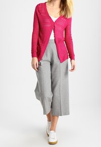 Magenta gebreid vest met open steekpatroon, gecombineerd met grijze culottes met hoge taille en witte sneakers. Eenvoudig ontwerp, casual pasvorm.