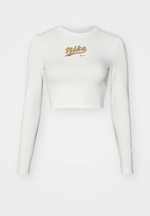 Crop top blanc à manches longues en tissu lisse, avec un imprimé doré du logo Nike sur la poitrine et un col rond classique.