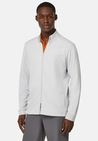 Chaqueta de color gris claro con cremallera, patrón texturizado, cuello alto y un interior naranja en contraste. Presenta un bolsillo en el pecho y puños acanalados.