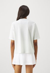 Ανοιχτό πράσινο, κοντομάνικο μπλουζάκι από διχτυωτό ύφασμα με άνετη εφαρμογή, που διαθέτει στρογγυλή λαιμόκοψη και λεία υφή. Συνδυάζεται με λευκή πλισέ φούστα.