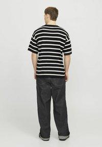 Stribet sort-hvid t-shirt med afslappet pasform, korte ærmer og rund halsudskæring, parret med mørk denimbukser med synlige sømme.