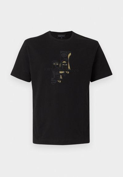 Μαύρο κοντομάνικο μπλουζάκι με αφηρημένα κατακόρυφα σχέδια μάσκας σε απαλό χρυσό και μαύρο, με το κείμενο "Emporio Armani" στο ύψος του στήθους.