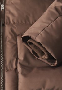 Doudoune marron avec une texture lisse et brillante, dotée d'un col en tricot marron retroussé et d'une fermeture éclair métallique.