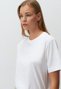 Weißes Baumwoll-T-Shirt mit runder Ausschnittform und kurzen Ärmeln. Der Stoff wirkt weich und glatt mit einer lockeren Passform.