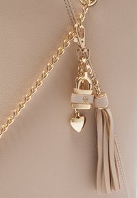 Beige handbag with textured leather, gold-tone chain strap, and decorative elements including a padlock and heart charm with a tassel.