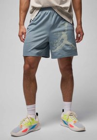 Lyseblå sportshorts med et struktureret netmønster og et grafisk print på venstre side. Kombineret med farverige sneakers og hvide sokker.