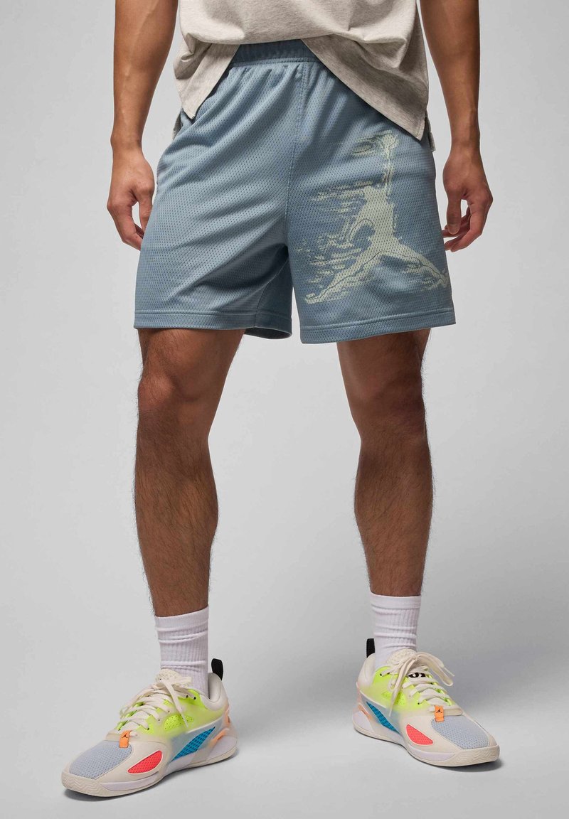 Lyseblå sportshorts med et struktureret netmønster og et grafisk print på venstre side. Kombineret med farverige sneakers og hvide sokker.
