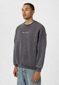 Grijze katoenen sweatshirt met geribde manchetten en zoom, met de tekst "Future Is Mine" in het wit geborduurd op de borst.