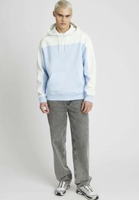 Haut à capuche bleu clair avec des manches blanches, poche avant et cordon de serrage. Associe à un jean gris et des baskets noir et blanc. Texture de tissu lisse.