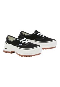 Schwarze Canvas-Sneaker mit einer dicken weißen Plateau-Sohle, brauner Gummisohle, weißen Schnürsenkeln und kontrastierenden weißen Nähten.