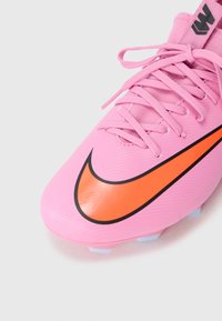Roze voetbalschoen met een oranje Nike swoosh, gestructureerd oppervlak en bijpassende veters. Heeft een gestroomlijnd ontwerp en gemolded studs.