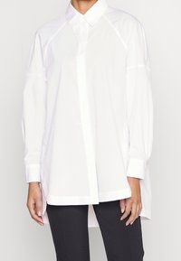 Hvid oversized knap-op skjorte lavet af glat bomuldsstof med spids krave, lange ærmer og ligefrem kant.