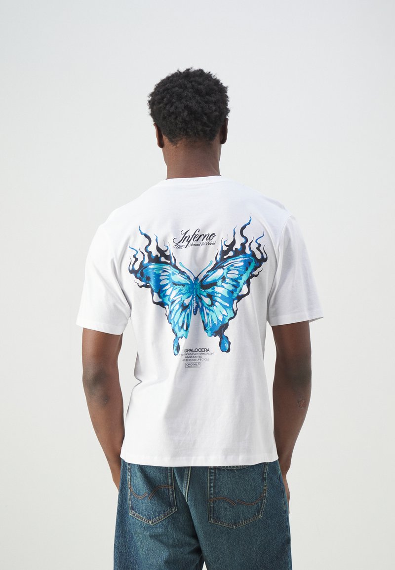 Witte katoenen t-shirt met een grote blauwe vlinderafbeelding met zwarte vlamaccenten op de achterkant. Korte mouwen en een relaxte pasvorm.