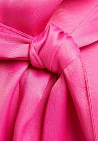 Jasnoróżny materiał, gładka textura, z węzłowym detalem na środku, z nakładającymi się warstwami i subtelnym połyskiem.