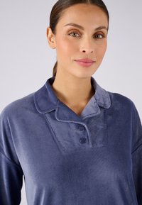 Suéter de pana azul marino con cuello, dos botones y un tejido texturizado. Presenta un diseño simple y limpio con un ligero brillo.