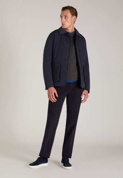 Veste matelassée marine avec un col, deux poches avant, portée avec un pull gris et un pantalon foncé, associés à des baskets marines.
