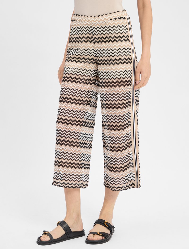 Krótkie spodnie w wzory z desenem w zygzak w odcieniach beżu, brązu i bieli, z czarnym paskiem po boku oraz luźnym fasonem.
