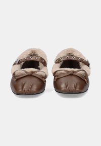 Zapatillas de cuero marrón con forro de piel de oveja beige, detalle de lazo pequeño en la parte frontal, correa ajustable con adornos plateados, diseño de punta redondeada.