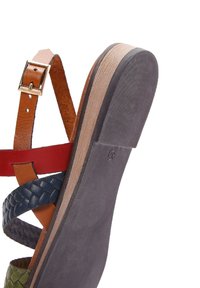 Sandale à lanières avec des bandes en cuir multicolores vert, bleu et rouge. Semelle en caoutchouc texturé avec un accent en bois au niveau du talon.