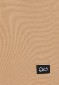 Tessuto a costine color tan con superficie testurizzata; presenta un piccolo etichetta nera con testo bianco nell'angolo in basso a destra.