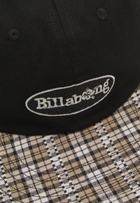 Juodas kepurė su smėlinės ir juodos spalvos languota kraštine, priekyje su išausta "Billabong" logotipu. Tekstūruota medžiaga.