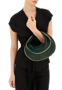 Borsa a mano verde in pelle dalla forma curva a mezzaluna, decorata con borchie dorate lungo il bordo, tenuta da una modella che indossa un outfit nero.