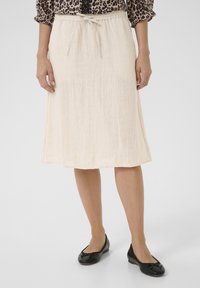 Fustă lungă până la genunchi, de culoare crem deschis, cu talie ajustabilă prin șnur. Material moale, texturat. Asortată cu pantofi negri cu talpă plată, cu un accent sub formă de fundiță.