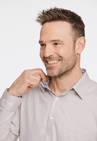 Jasnoszara koszula zapinana na guziki, wykonana z teksturowanej tkaniny, z kwiatowym nadrukiem na wewnętrznej stronie kołnierzyka i mankietów. Posiada kieszeń na piersi.