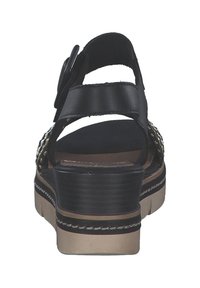 Black leather sandal with adjustable buckle closure, textured strap, and a chunky platform sole featuring a contrasting beige and black design.